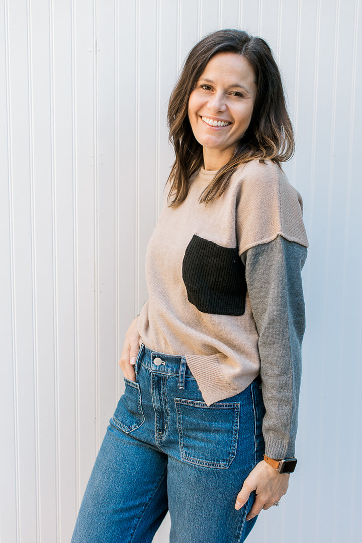 Model wearing a camel sweater with gray sleeves with exposed hem at sleeve.