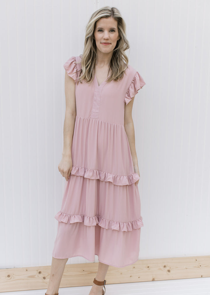 Model is wearing heels with a blush colored midi with ruffled tiers and ruffle cap sleeves.