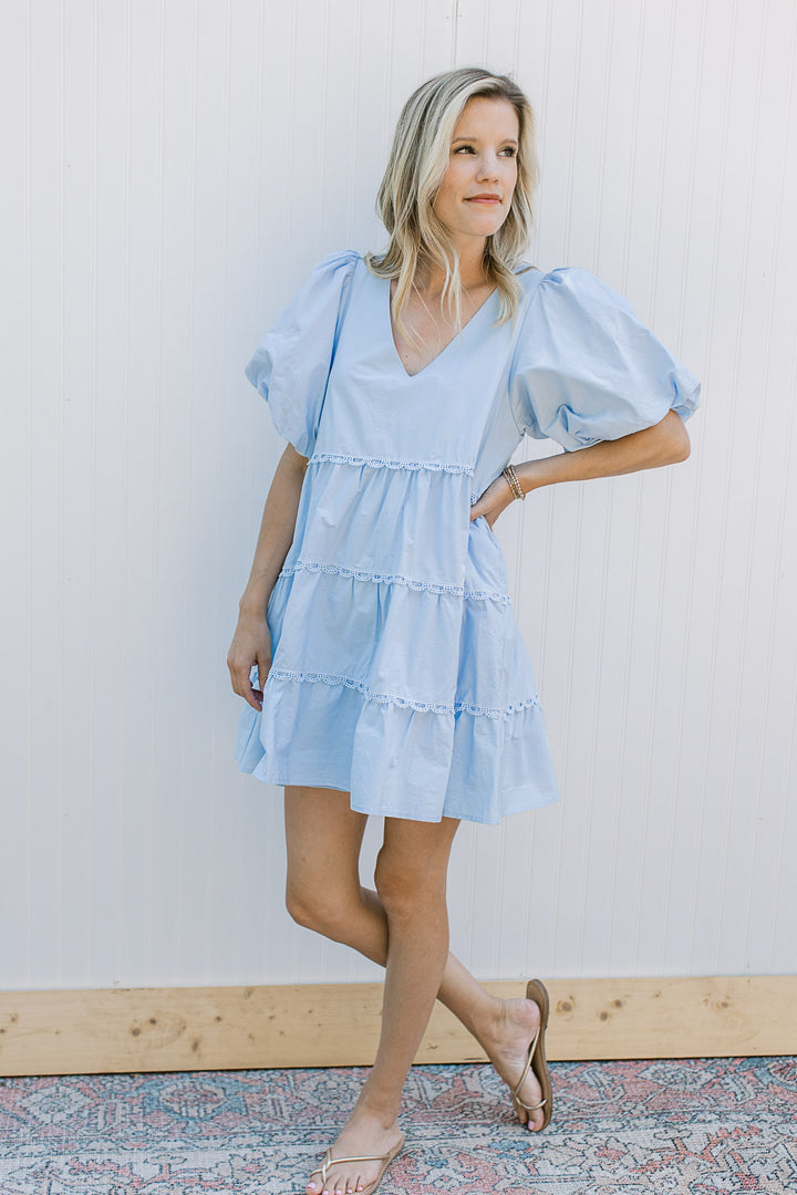Model wearing a baby blue dress with lace lined tiers and bubble short sleeves.
