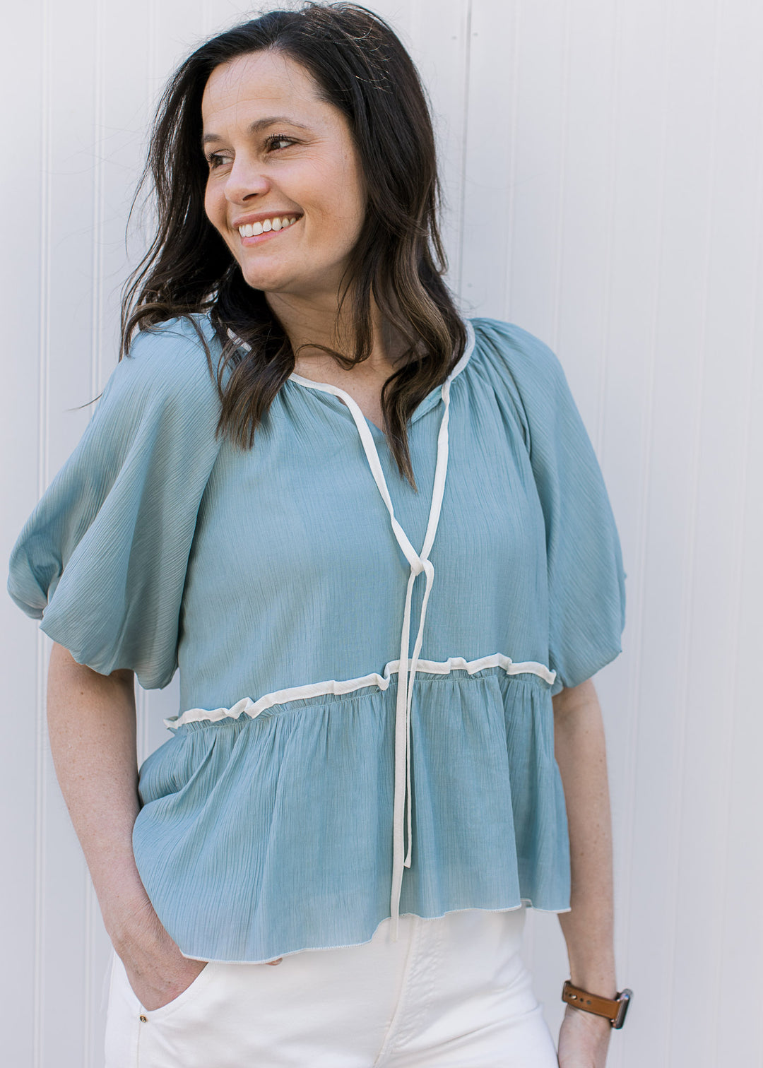 Model wearing a soft blue top with cream detailing, v-neck with a tie and short bubble sleeves.