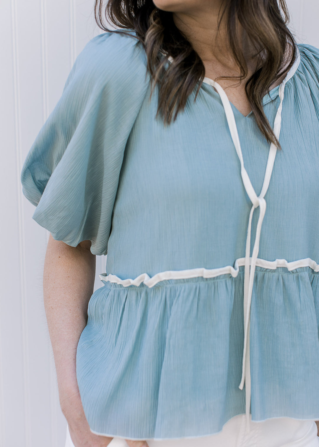 Close up of bubble short sleeve and v-neck with a tie on a soft blue top with cream detail.