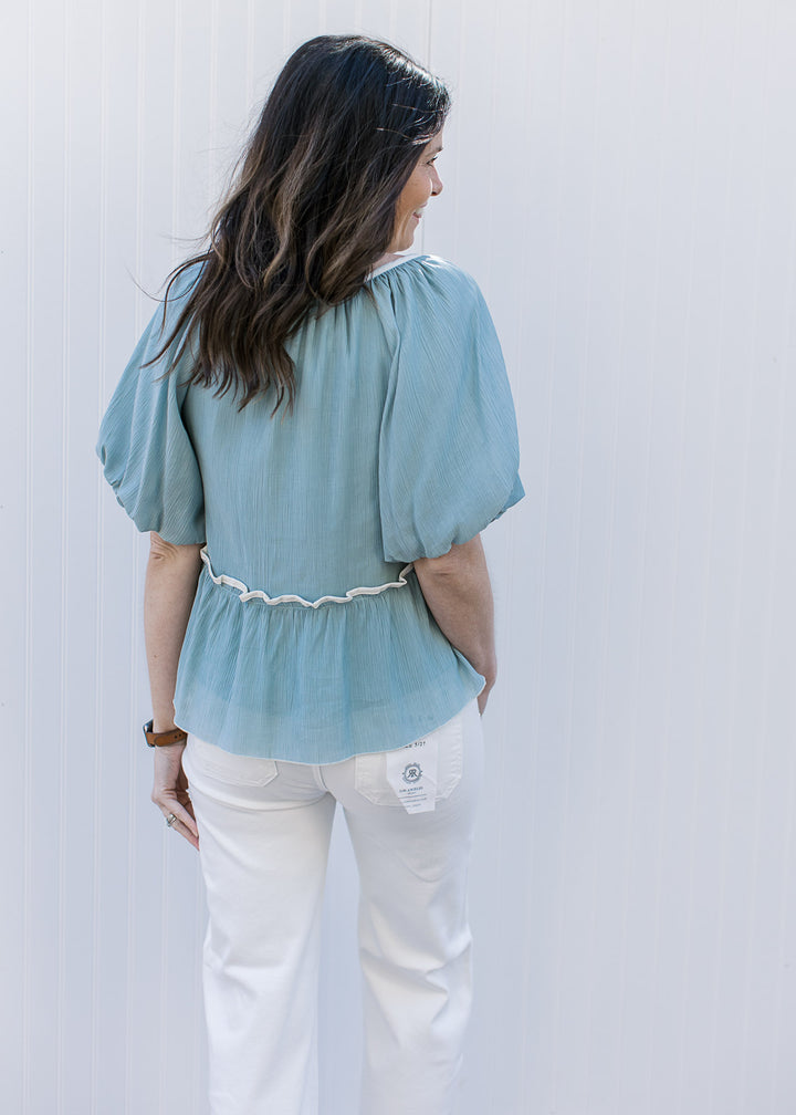 Back view of Model wearing a soft blue top with cream detailing, babydoll fit and short sleeves.
