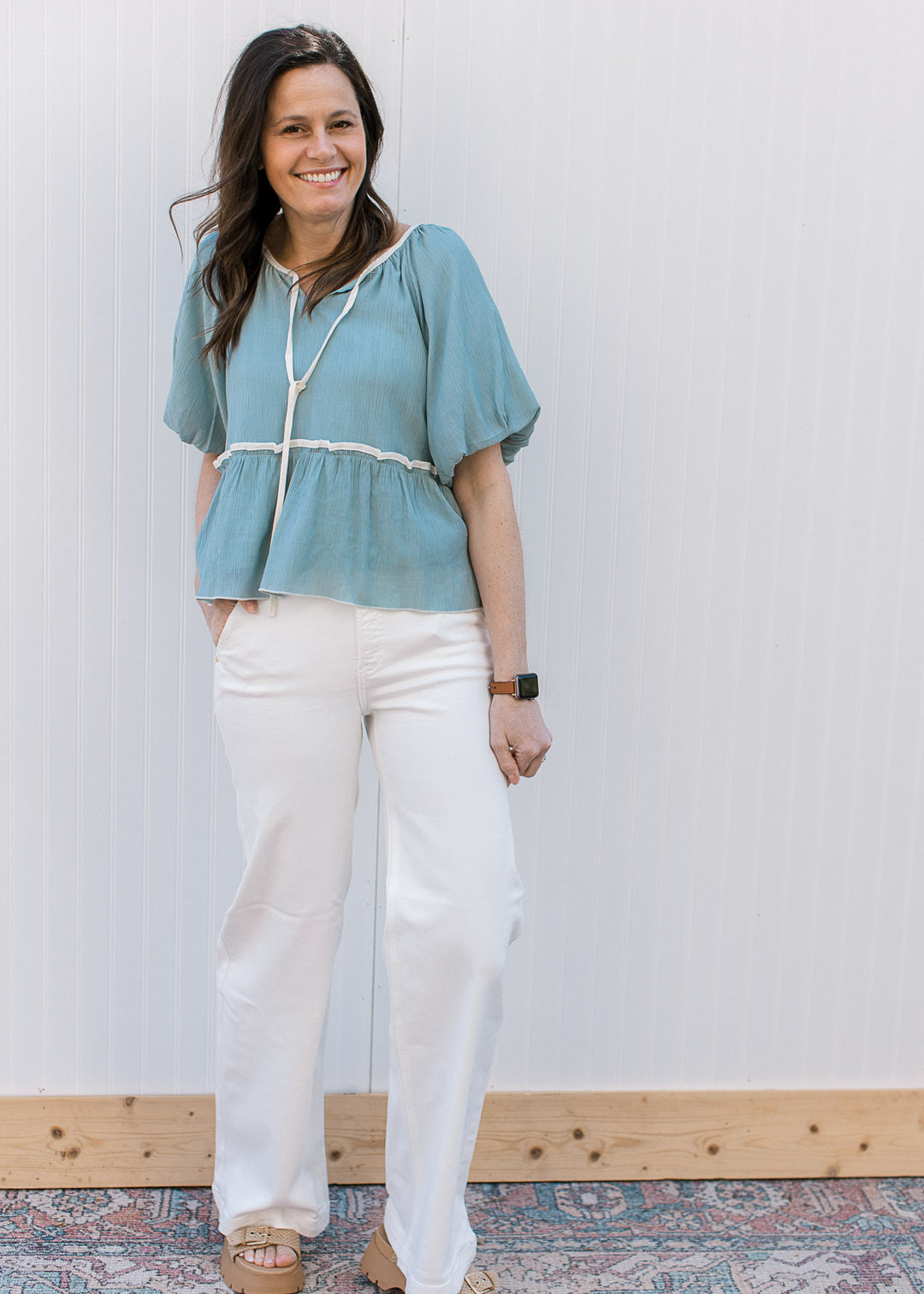 Model wearing white pants and a soft blue top with cream detailing and short bubble sleeves.
