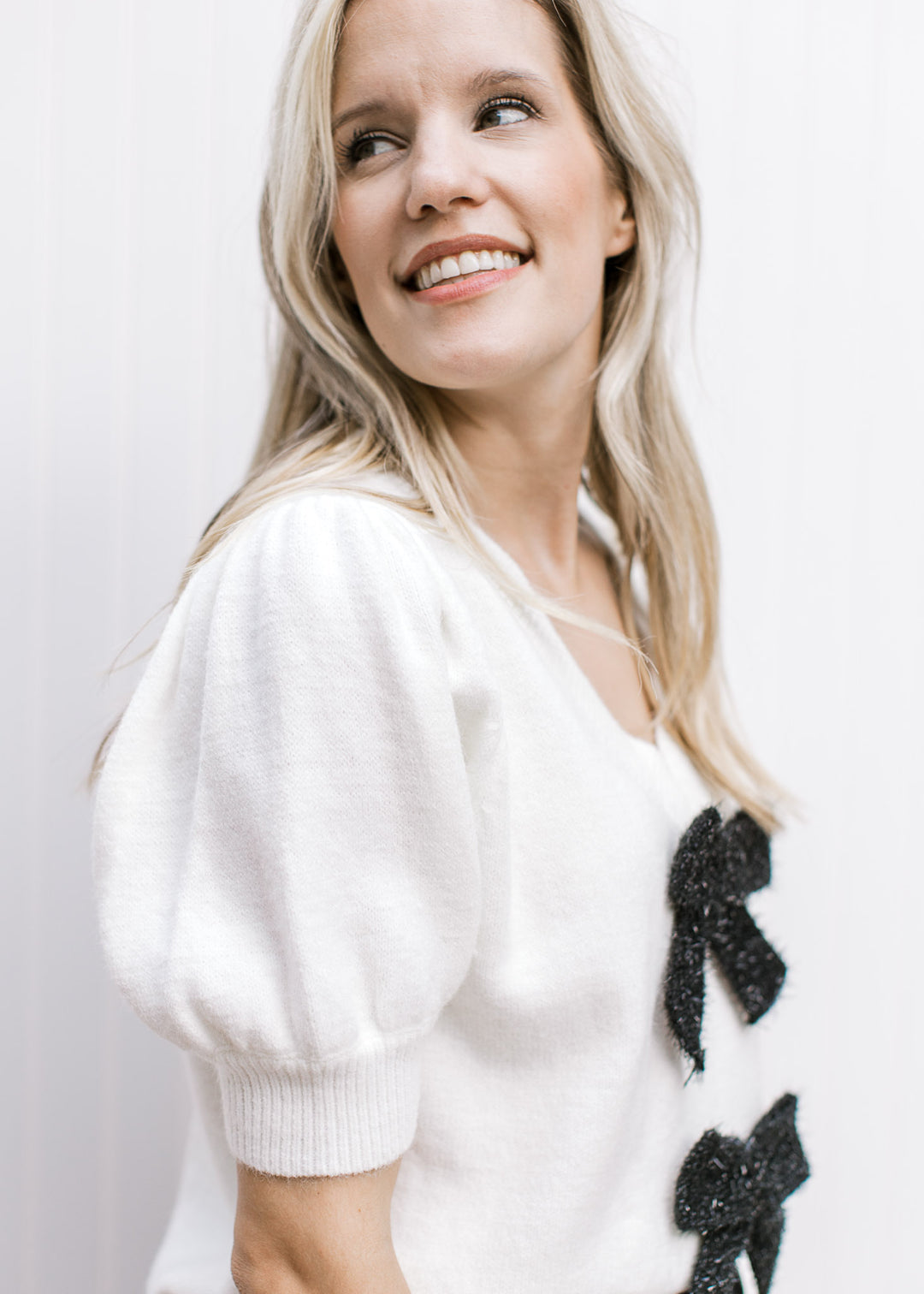 Close up of short puff sleeves and v-neck on a cream top with two black shimmer bows.