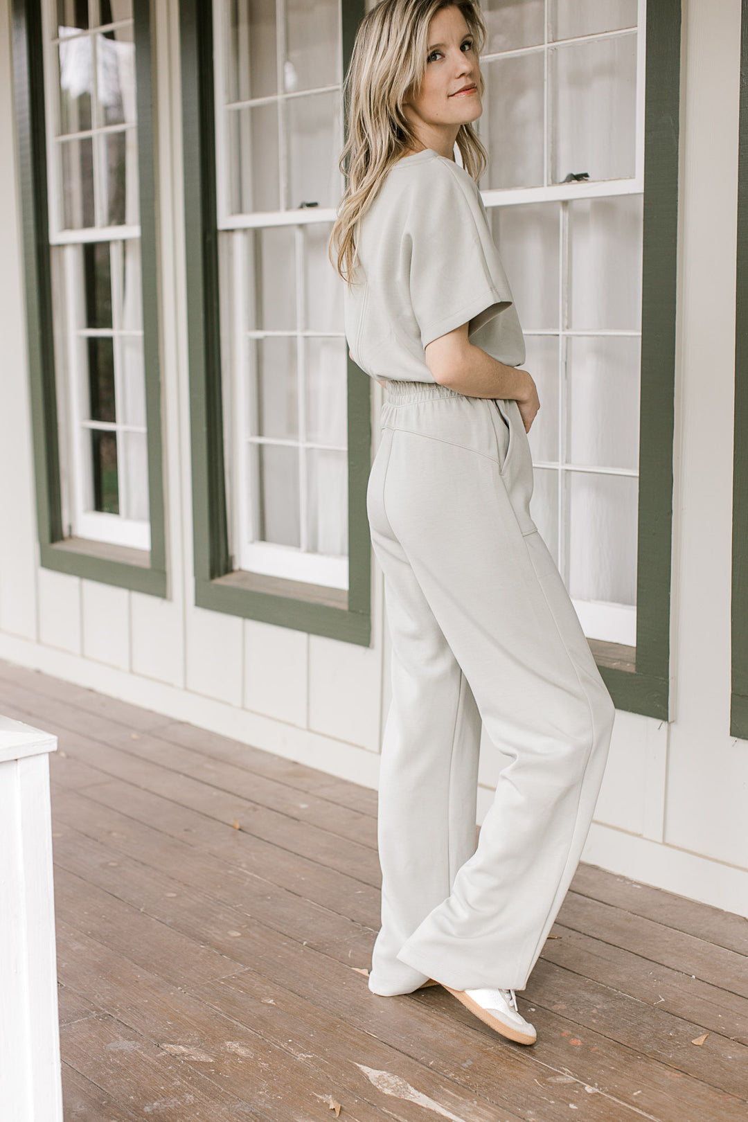 Side view of model wearing a sage jumpsuit with an elastic waist and short sleeves.
