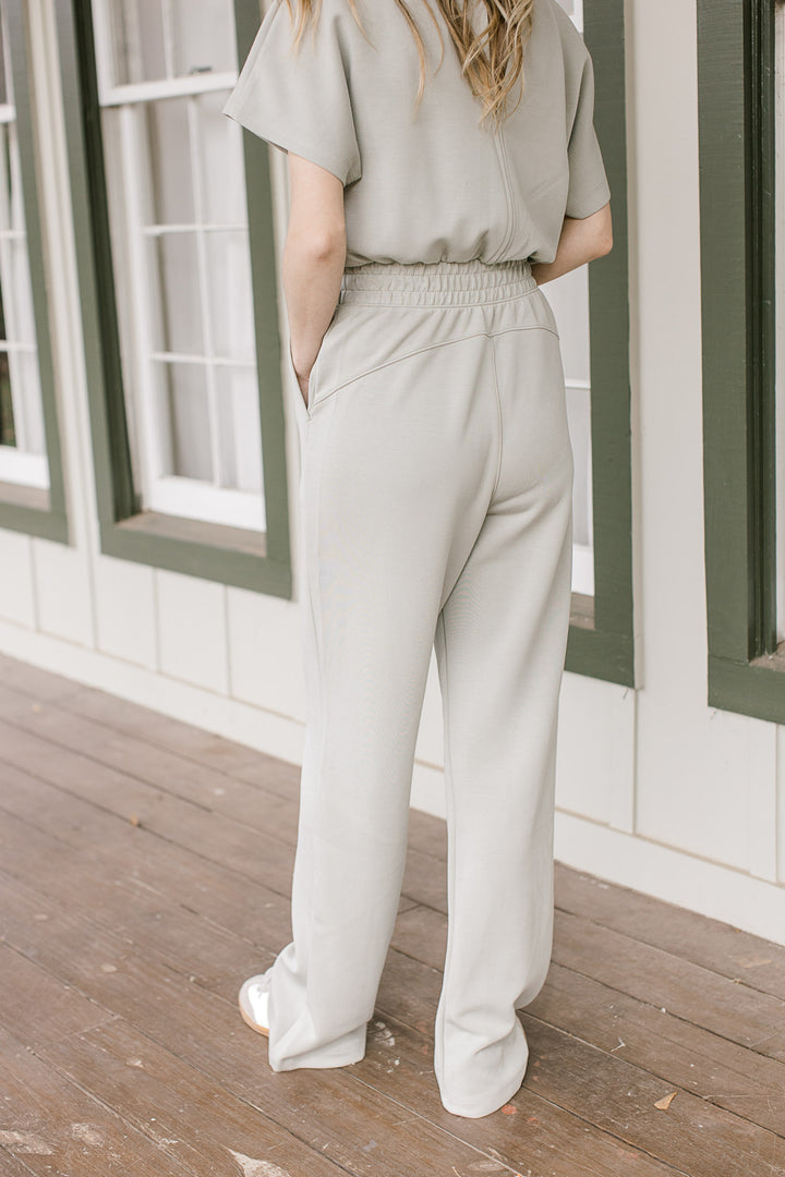Back view of elastic waist and pockets on a sage jumpsuit with short sleeves and button closure.