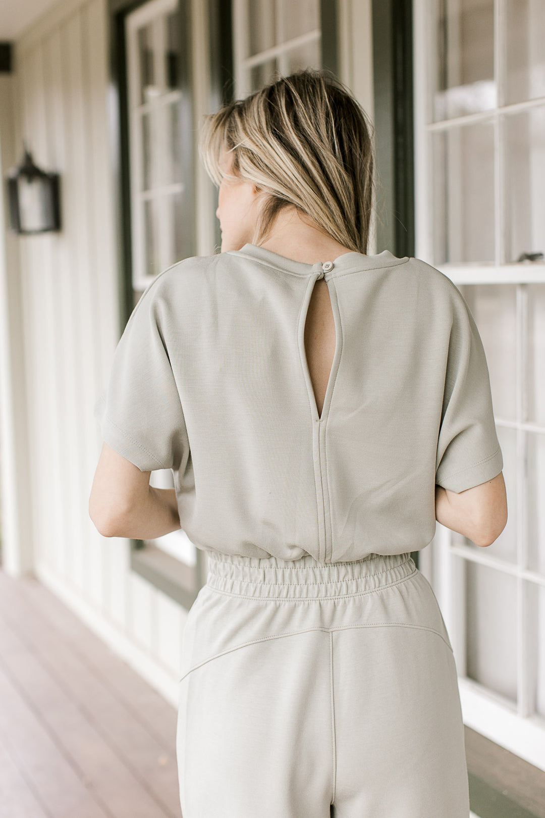 Close up of single button closure and short sleeves on a sage jumpsuit with an elastic waist.