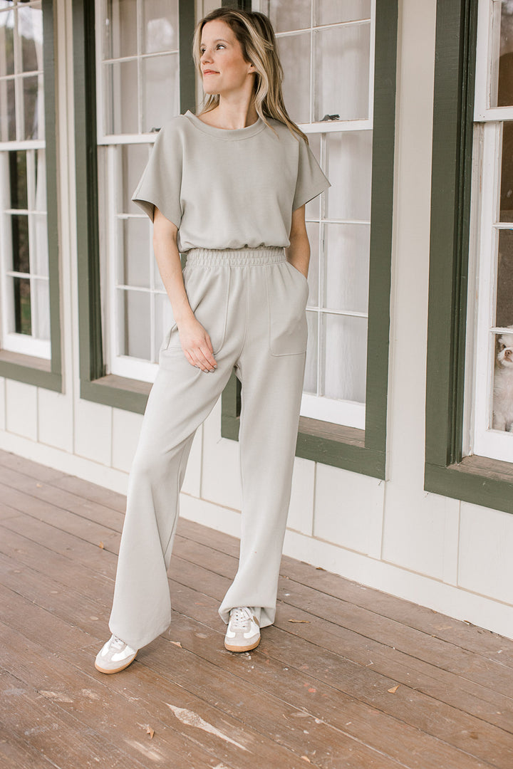 Model wearing a sage jumpsuit with an elastic waist, short sleeves and a single button closure.