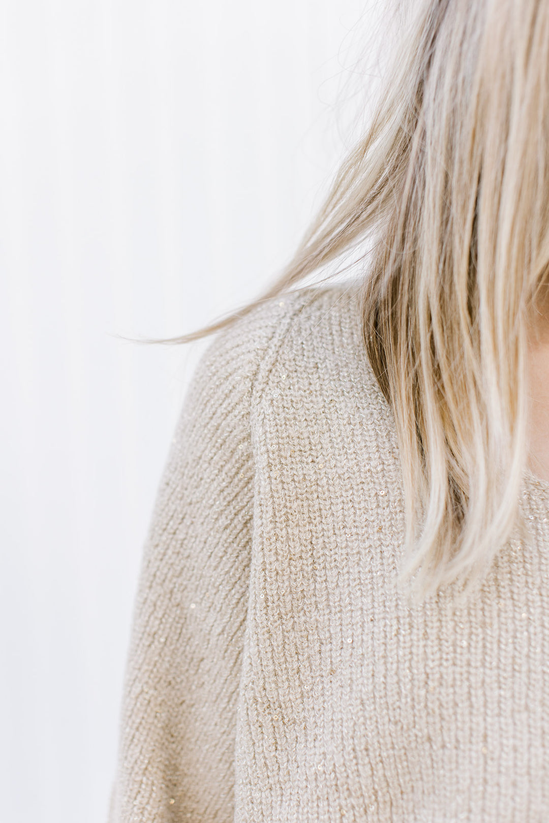 Close up of sparkles woven into a medium knit champagne sweater with long sleeves and a v-neck.