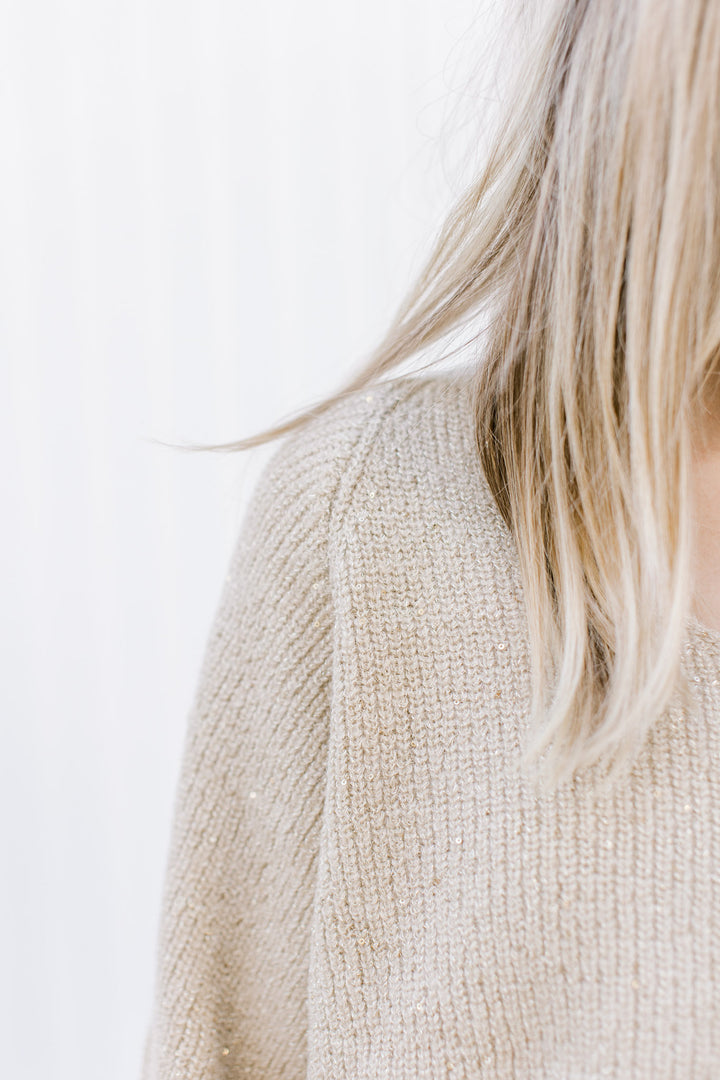 Close up of sparkles woven into a medium knit champagne sweater with long sleeves and a v-neck.