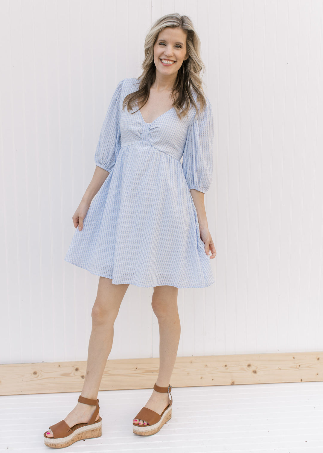 Model wearing heels with a pale blue tone on tone checkered dress with a placket at bodice.