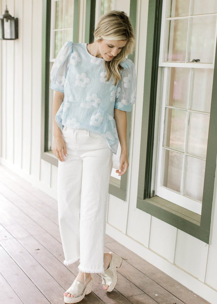 Model wearing a light blue babydoll top with stitched flowers and sheer bubble short sleeves.
