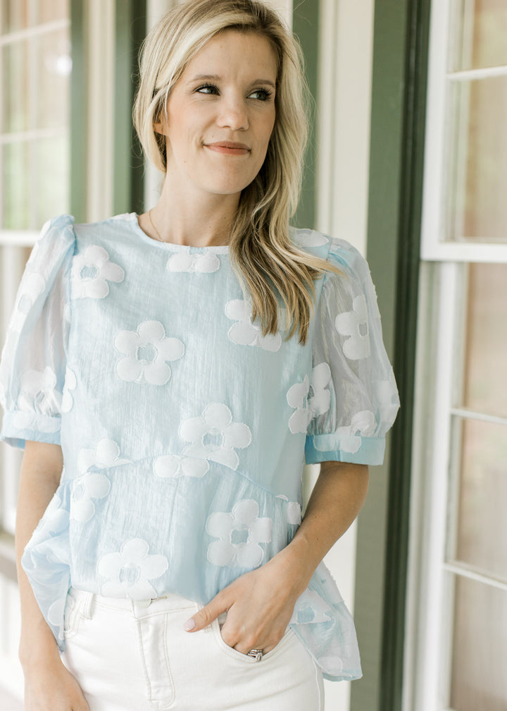 Model wearing a light blue top with textured flowers and short sleeves.