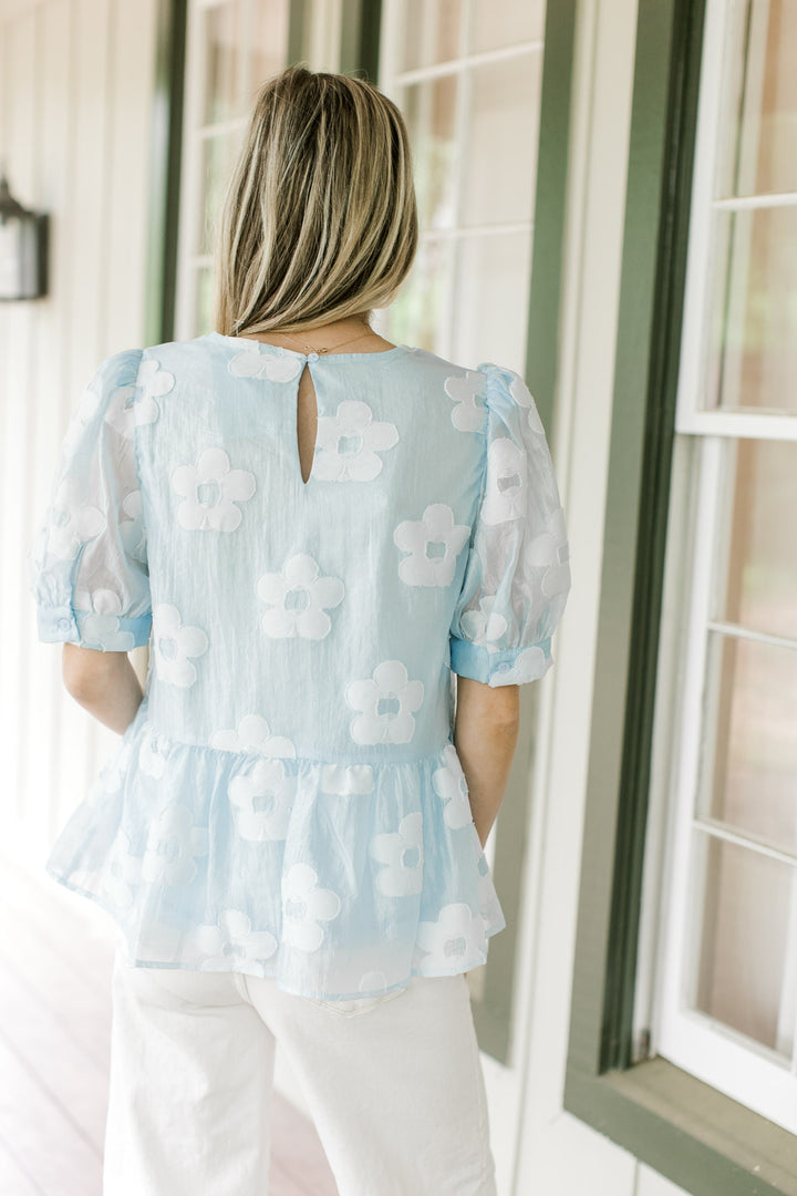 Back view of Model wearing a light blue babydoll top with stitched flowers and keyhole closure.