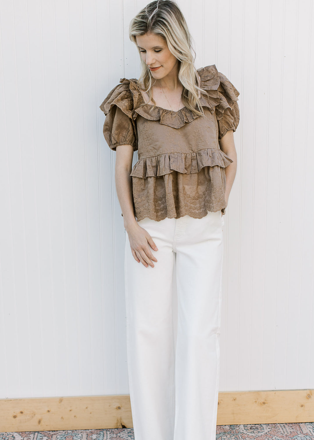 Model wearing a golden brown short sleeve top with ruffles at neck, sleeve and waist.