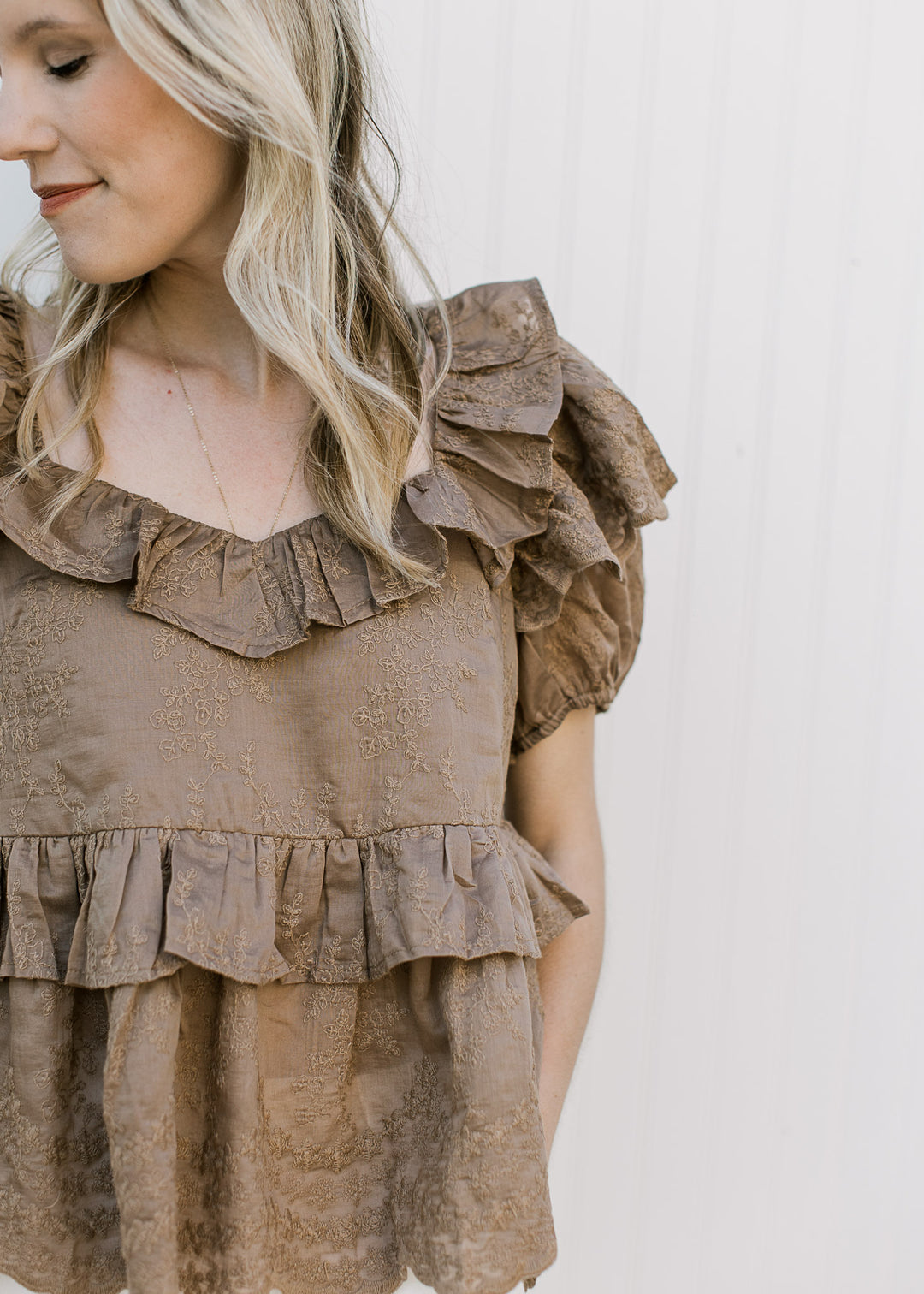Close up of ruffles at neck, sleeve and waist on a golden brown short sleeve top with v-neck.