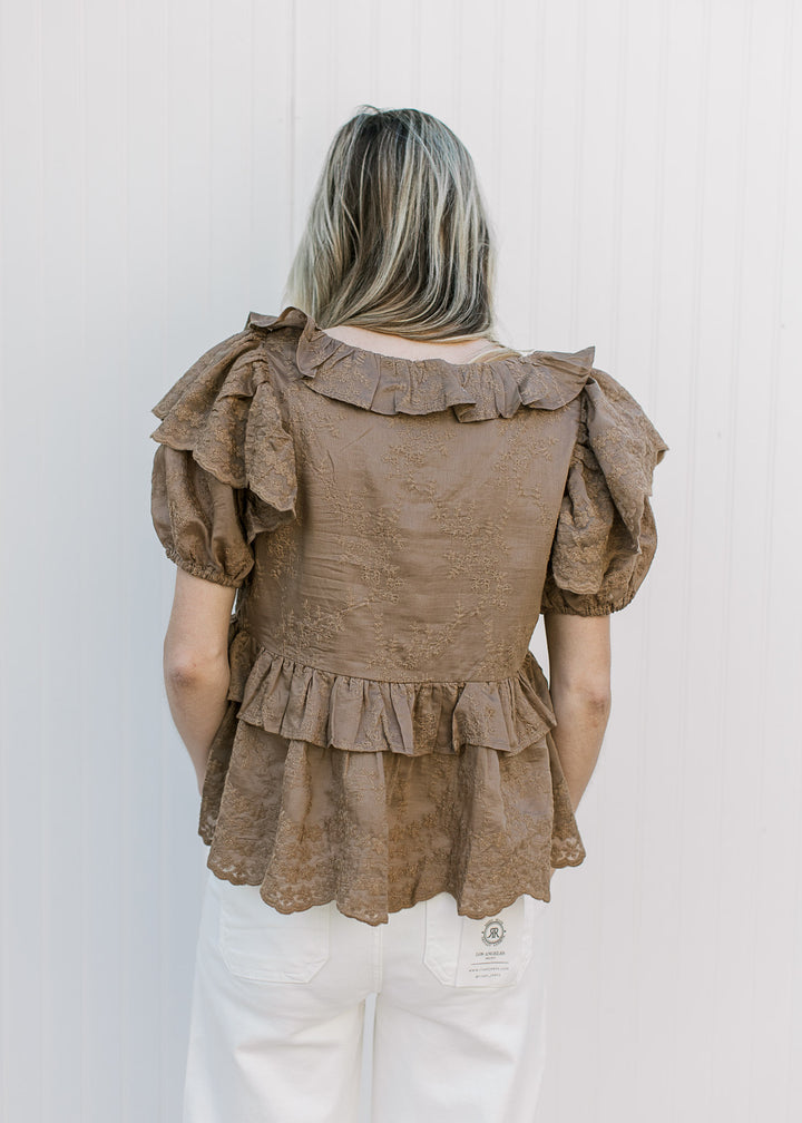 Back view of Model wearing a golden brown top with short sleeves and ruffle details.
