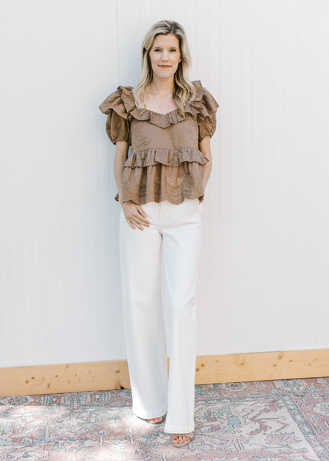 Model wearing white pants and a golden brown top with embroidered floral and short sleeves.