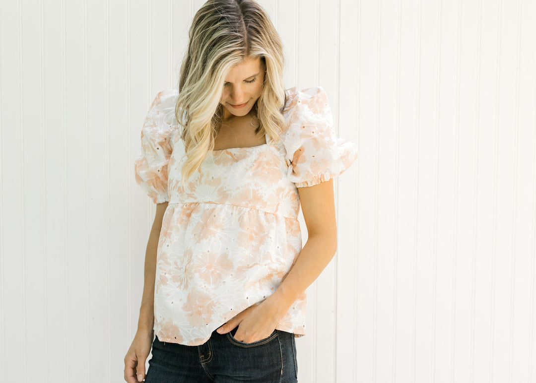 Model wearing a white and coral embroidered floral top with eyelets and bubble short sleeves.