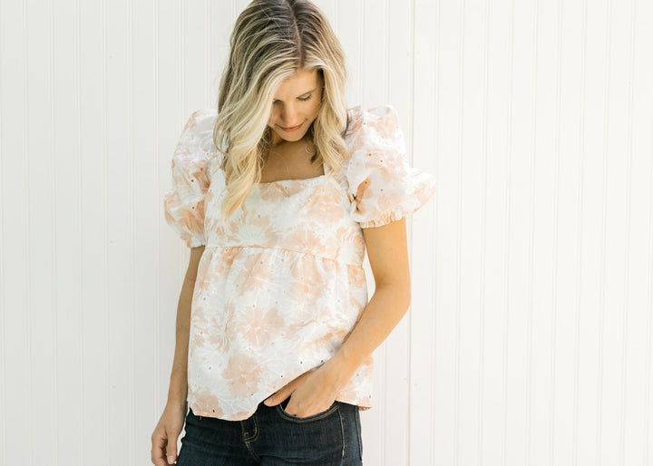 Model wearing a white and coral embroidered floral top with eyelets and bubble short sleeves.
