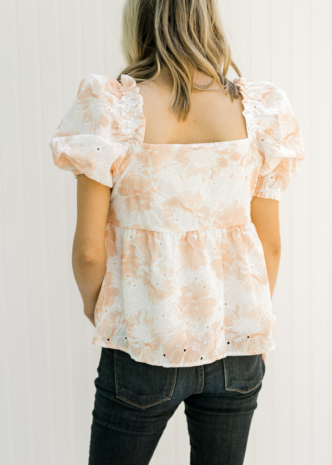 Back view of Model wearing a white and coral embroidered floral top and bubble short sleeves.