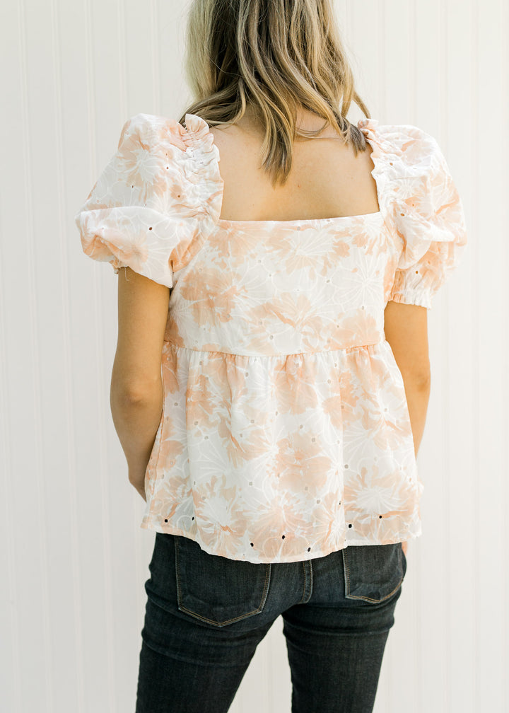 Back view of Model wearing a white and coral embroidered floral top and bubble short sleeves.