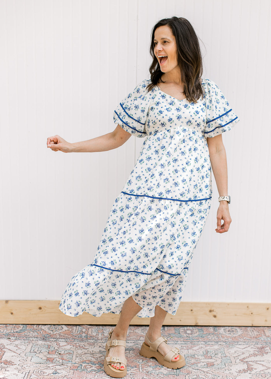 Model wearing sandal and a cream maxi with blue floral, bubble short sleeves, v-neck and pockets.