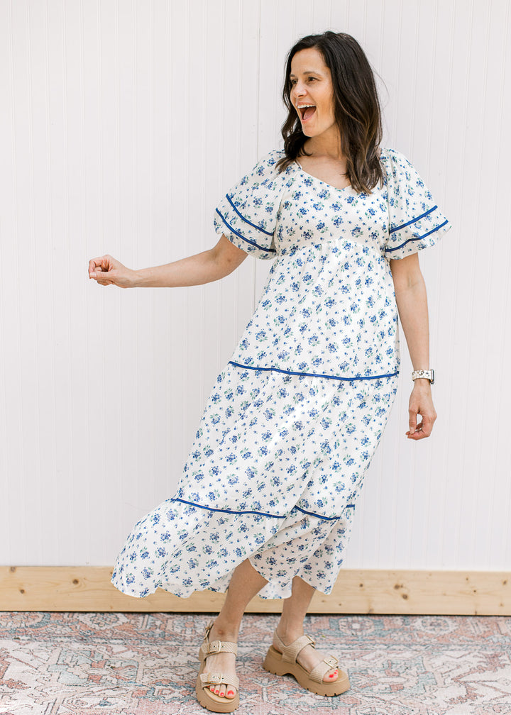 Model wearing sandal and a cream maxi with blue floral, bubble short sleeves, v-neck and pockets.