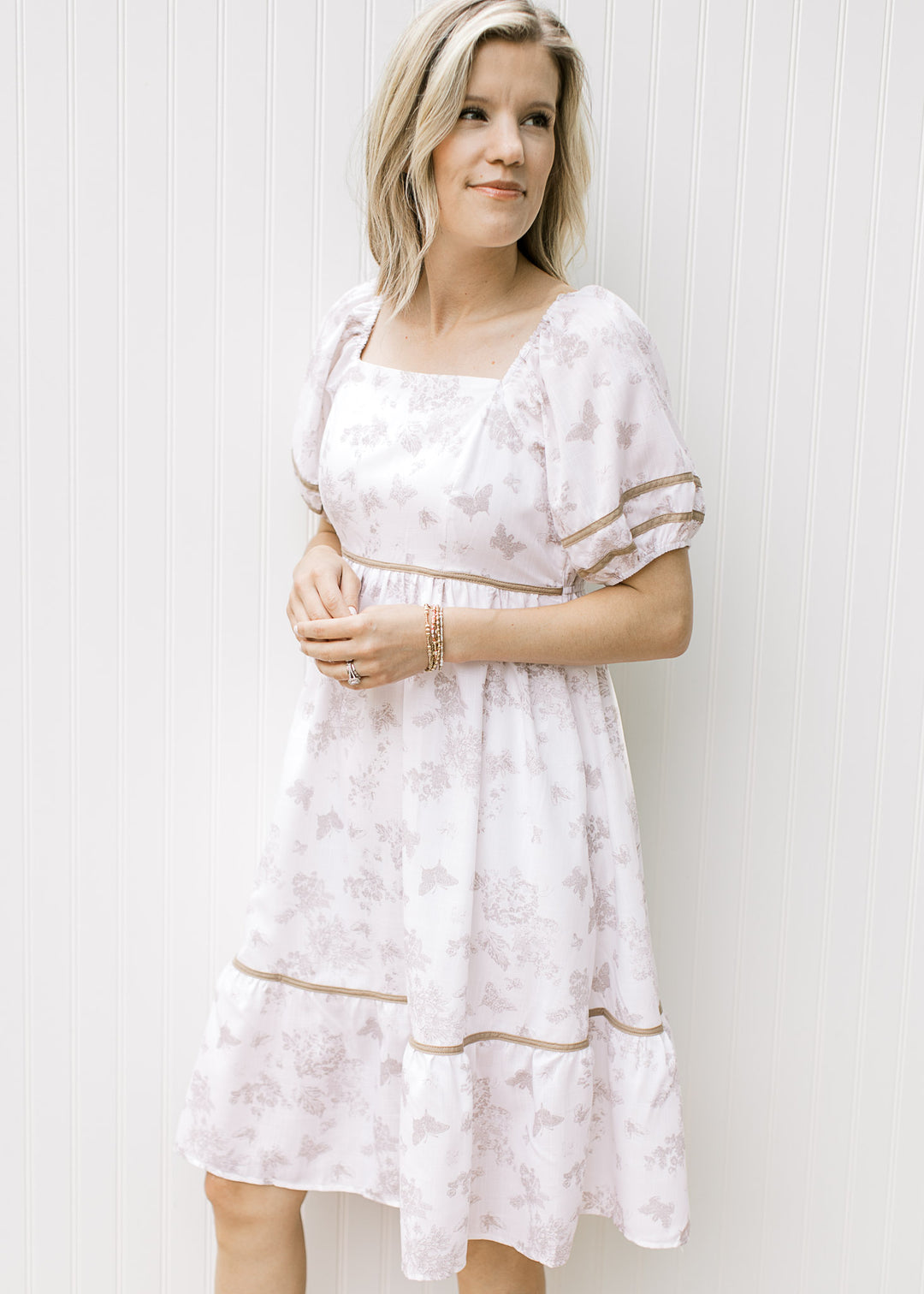 Model wearing a cream dress with wheat color piping, square neck and bubble short sleeves.