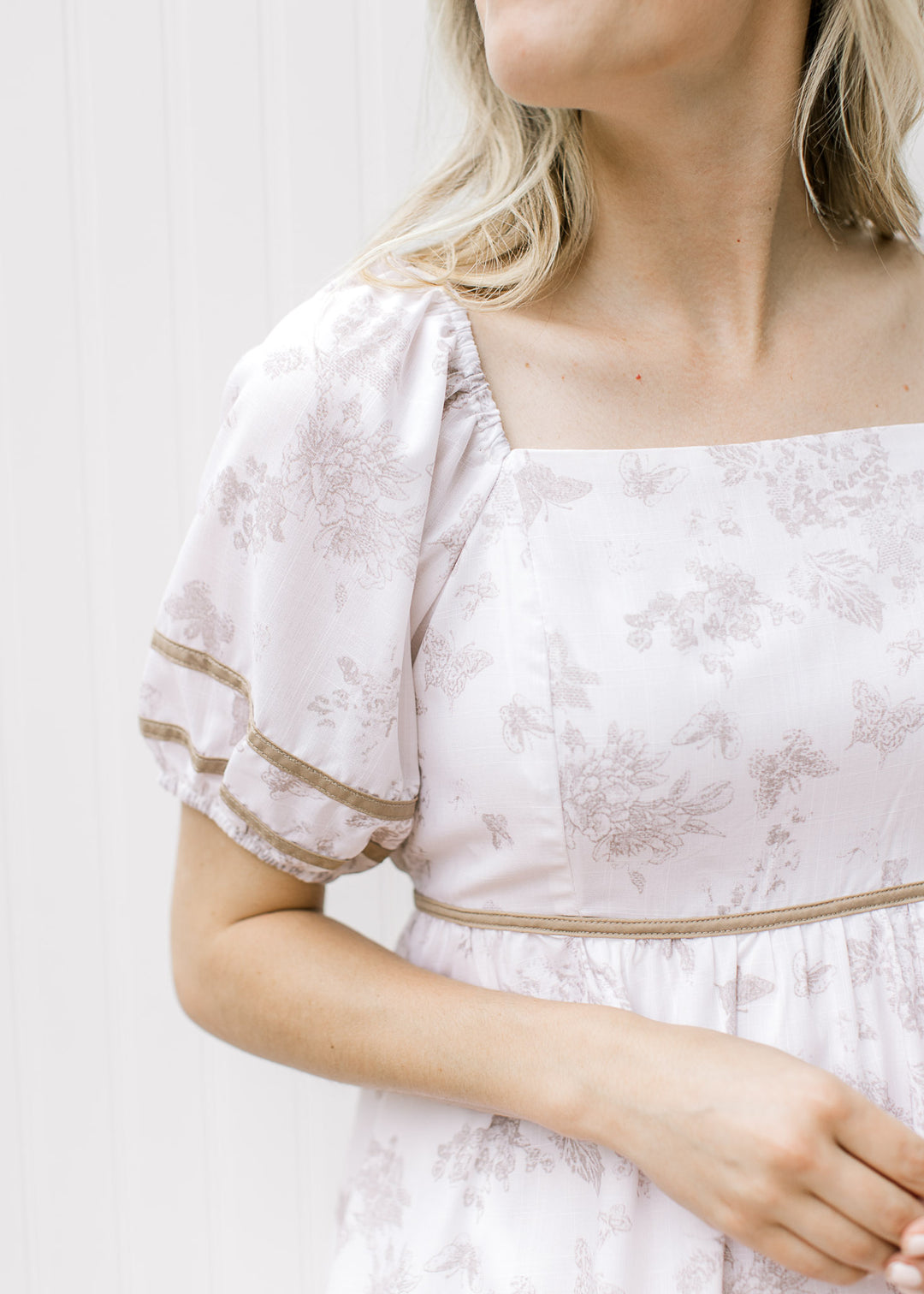 Close up of bubble short sleeves and square neck on a cream dress with butterflies and floral.