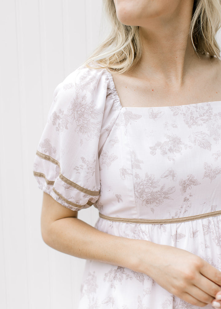 Close up of bubble short sleeves and square neck on a cream dress with butterflies and floral.