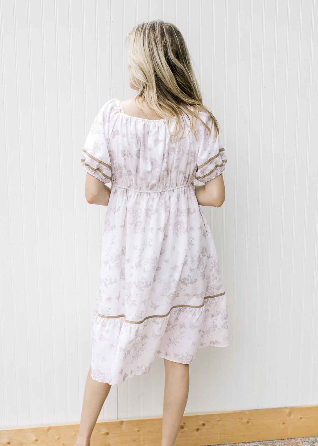 Back view of Model wearing a cream dress with wheat piping, square neck and bubble short sleeves.