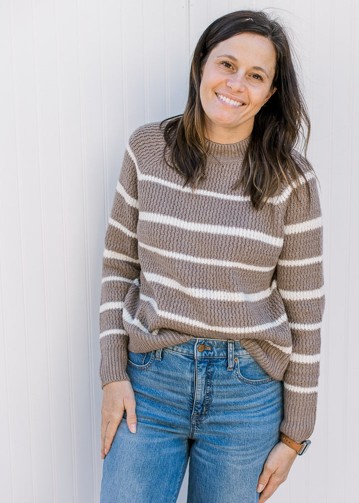 Model wearing jeans and a taupe sweater with white stripes, with long sleeves and a ribbed material.