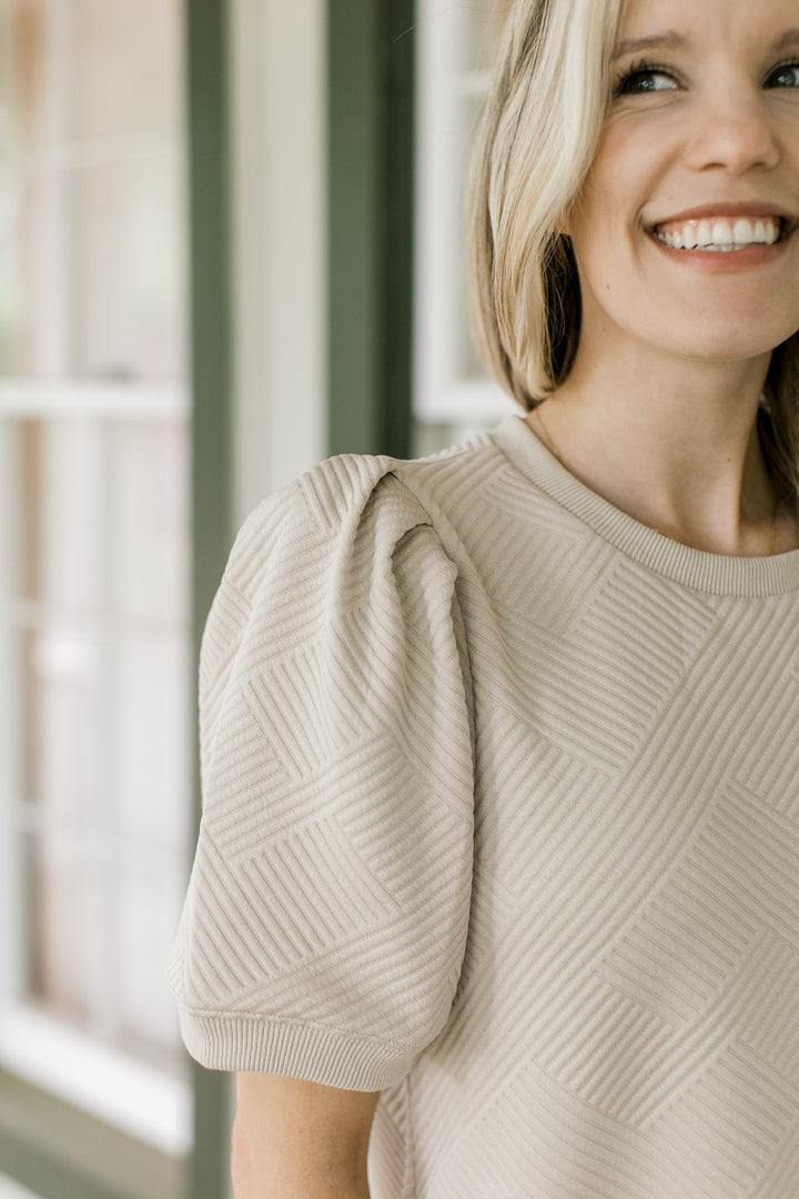 Close up of embossed pattern and pleated short sleeves on a taupe above the knee dress.