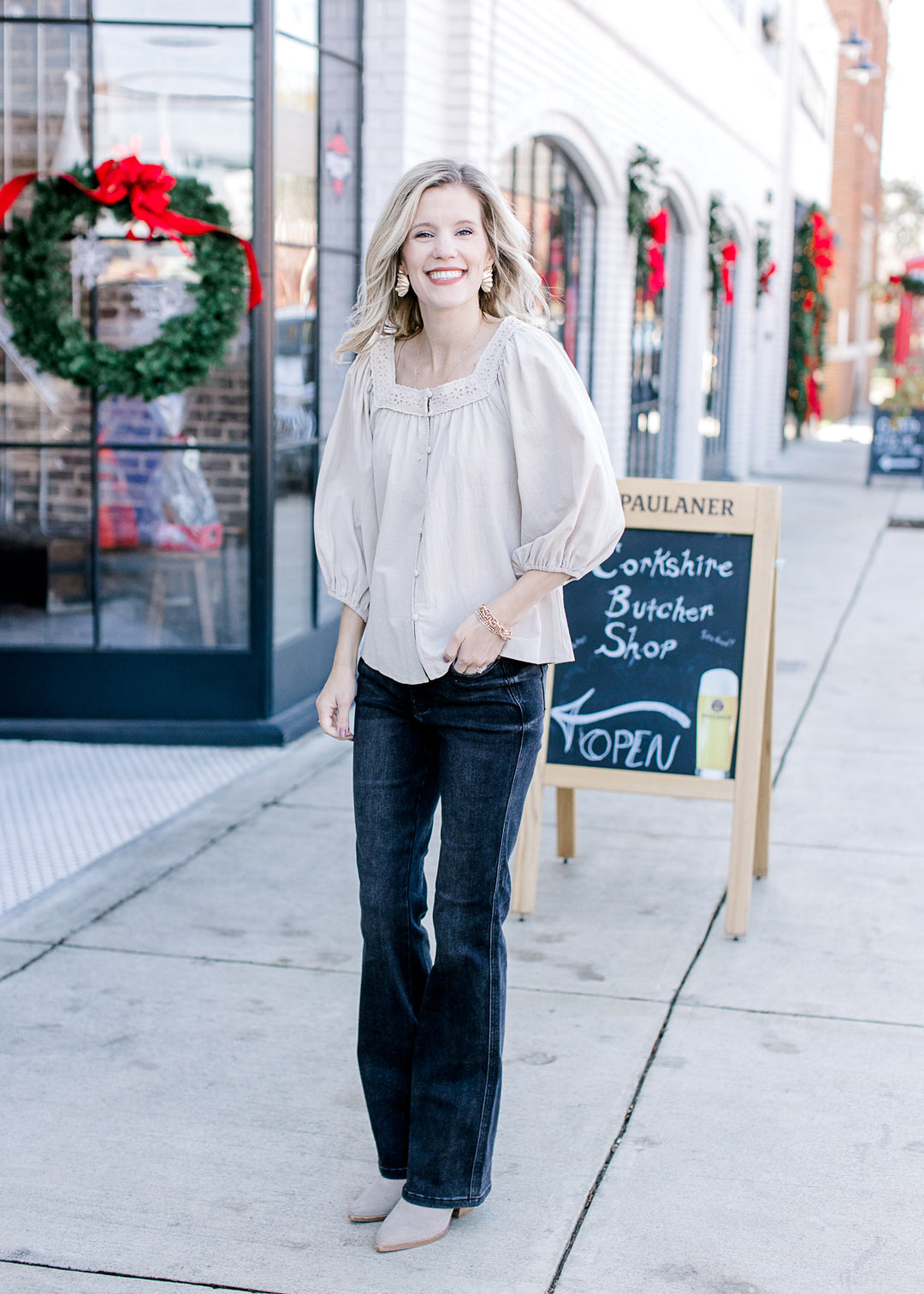 Model wearing jeans, boots and a taupe top with eyelet lace detail at neck and 3/4 sleeves.