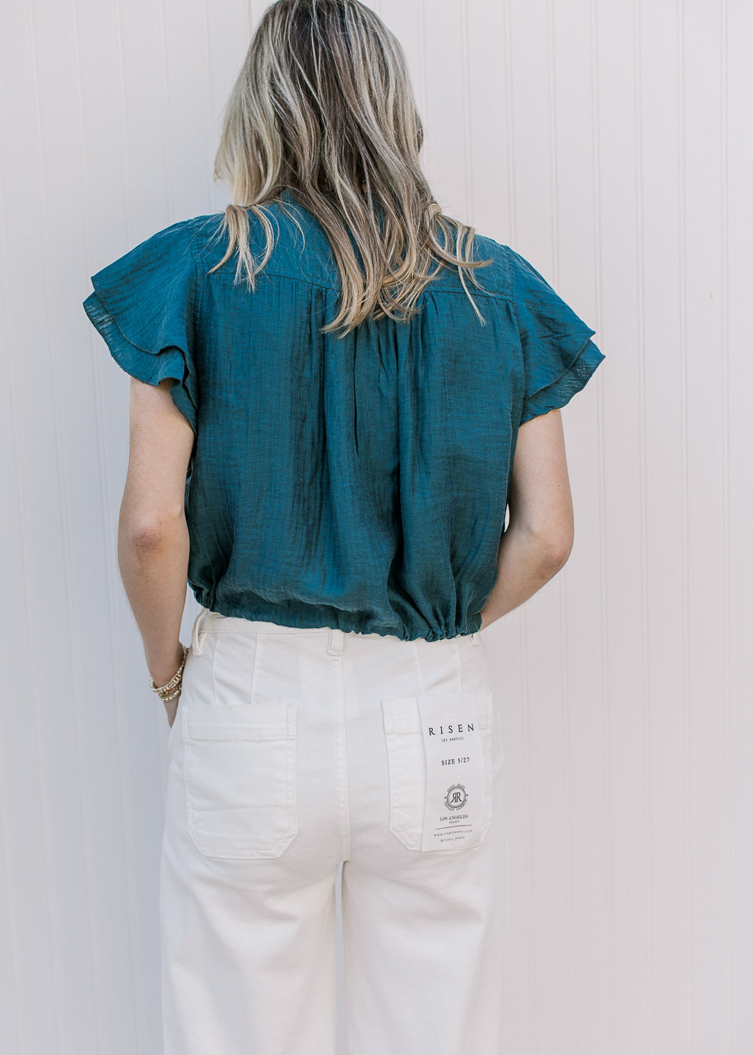 Back view of Model wearing a teal cropped top with double ruffle cap sleeves.