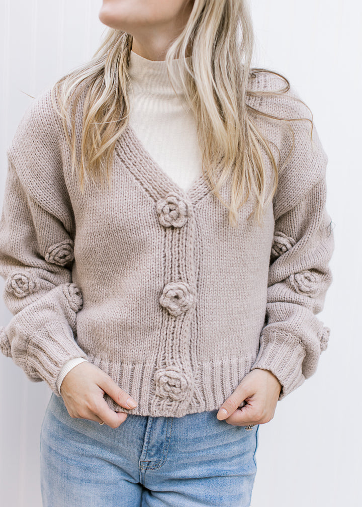 Close up of floral knit flowers on an oatmeal cardigan with long sleeves.