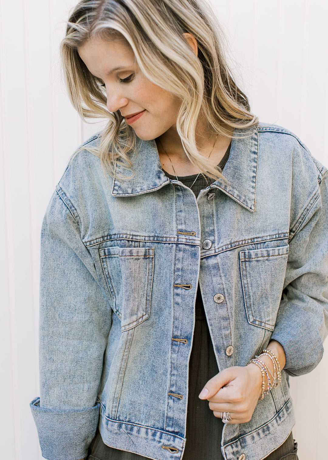 Model wearing a button up, light wash denim jacket with long sleeves and patch pockets.