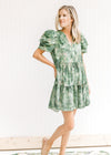 Model wearing an above the knee v-neck dress with a green and cream pattern and layered short sleeve