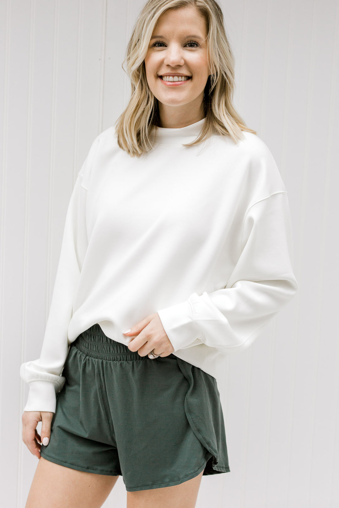 Blonde model wearing a cream sweatshirt with hunter green shorts.