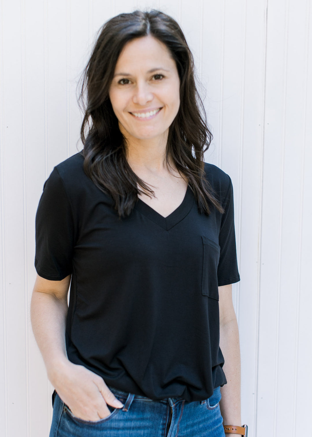 Model wearing a black, v-neck, short sleeve top with a chest pocket.