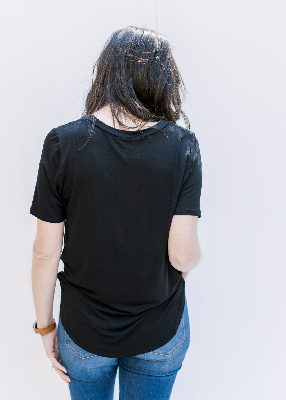 Back view of Model wearing a black, v-neck, short sleeve top with a chest pocket.