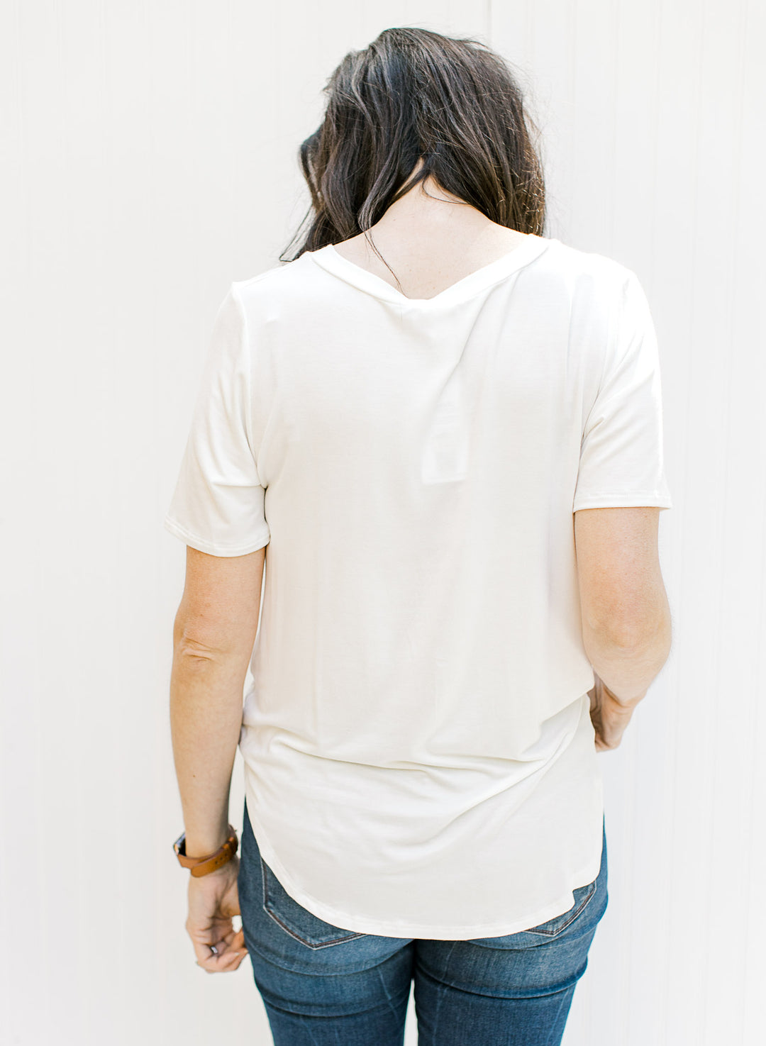 Back view of Model wearing a ivory colored short sleeve v-neck tee with a chest pocket.