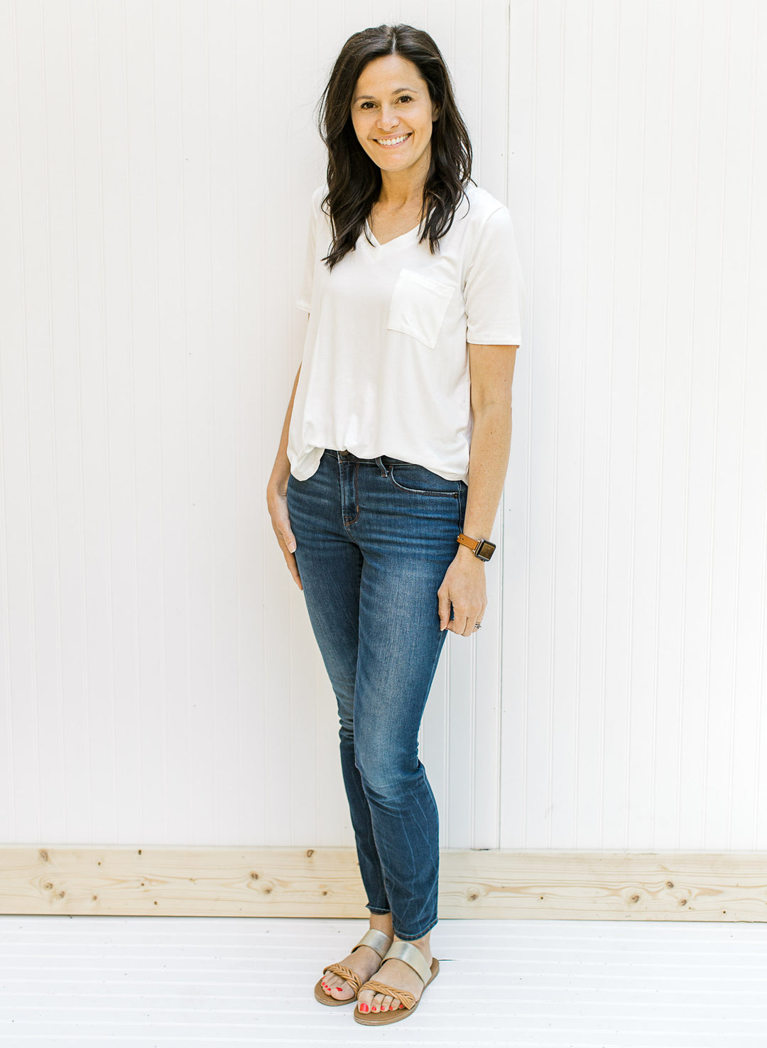 Model wearing a ivory colored short sleeve v-neck tee with a chest pocket with jeans and sandals.