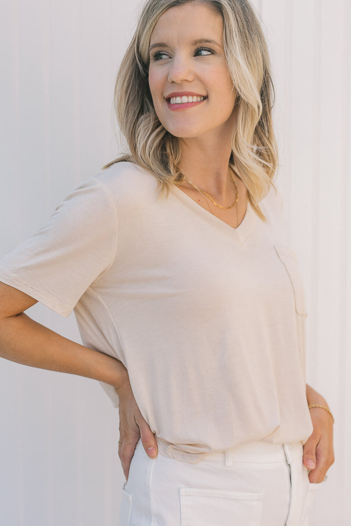 Model wearing a cream, v-neck,  short sleeve tee with a front pouch pocket