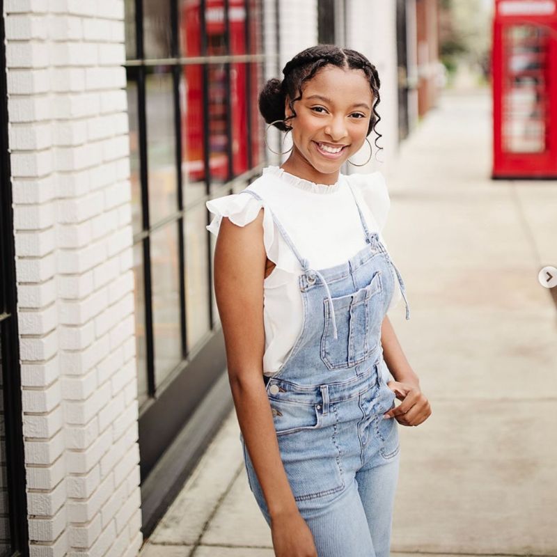 Young black woman wearing overalls and white shirt.