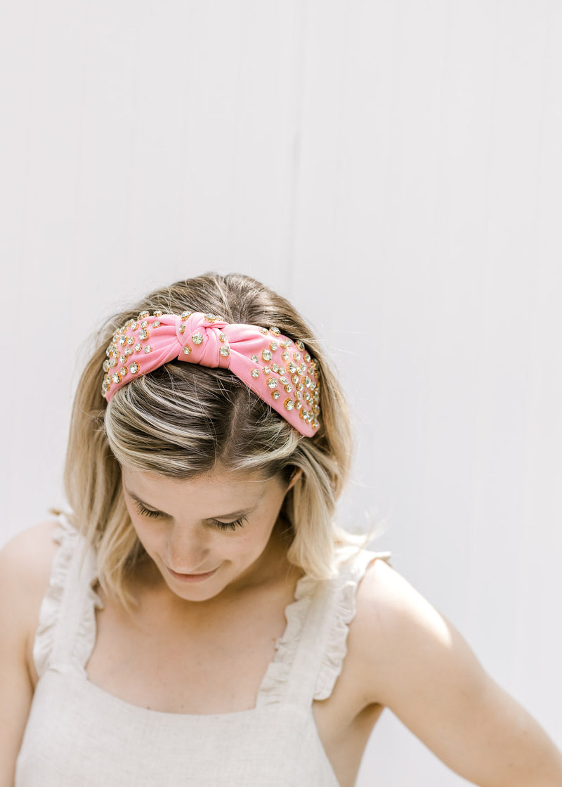 Top view of model wearing a pink bejeweled headband with a knotted fabric design. 