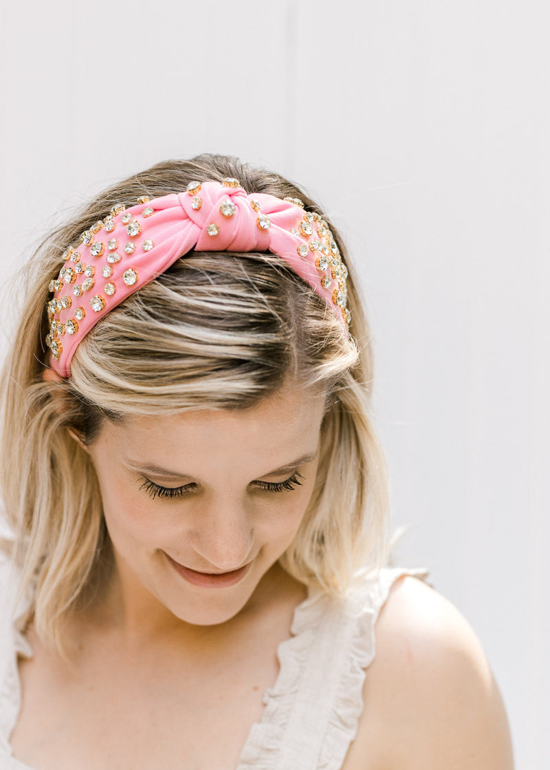Model wearing a pink headband with a knotted fabric and rhinestone design. 