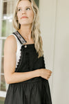 Close up of adjustable straps and bib pocket on a black maxi overall dress.