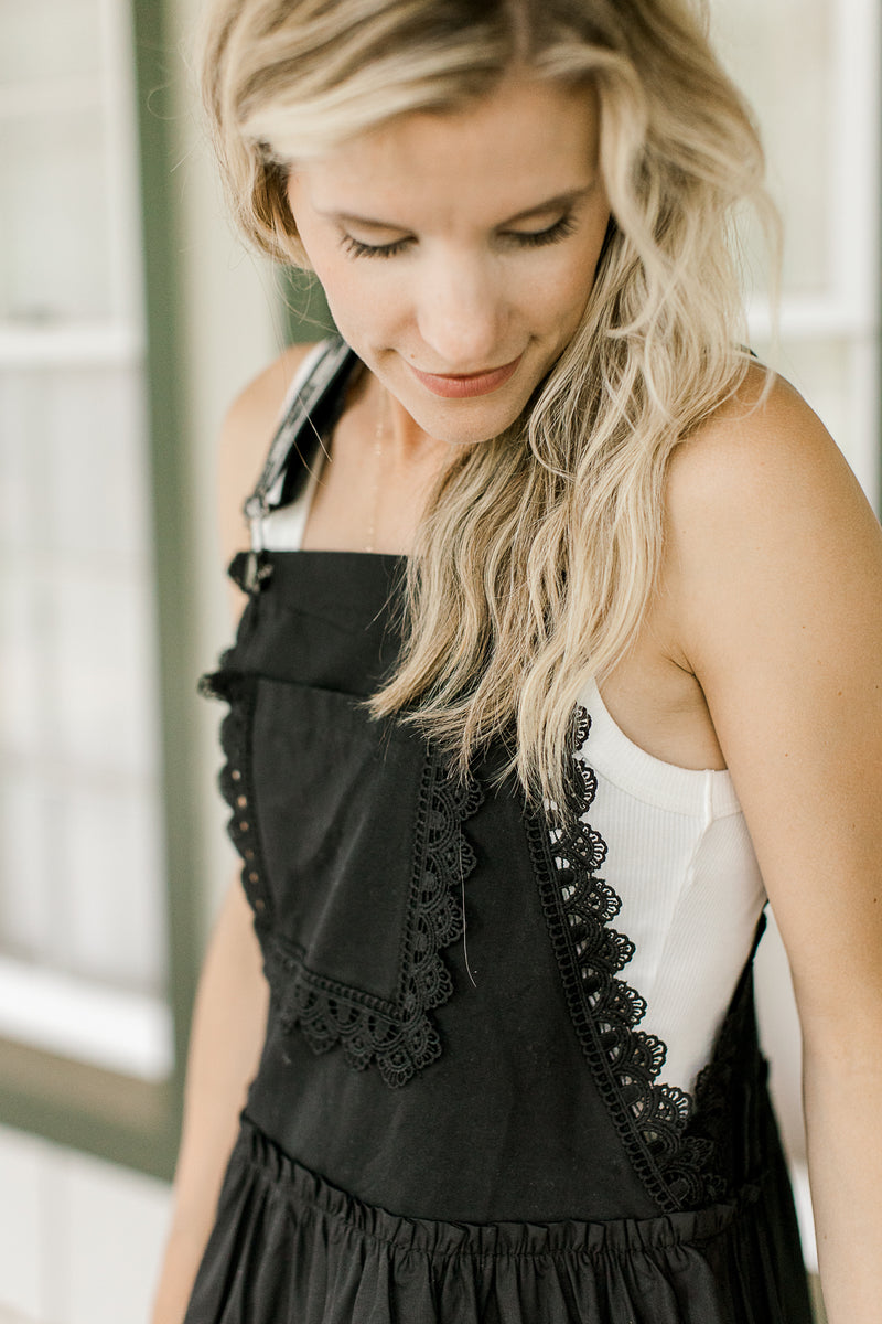 Model wearing a white top with black overall maxi with adjustable straps and a square neck.